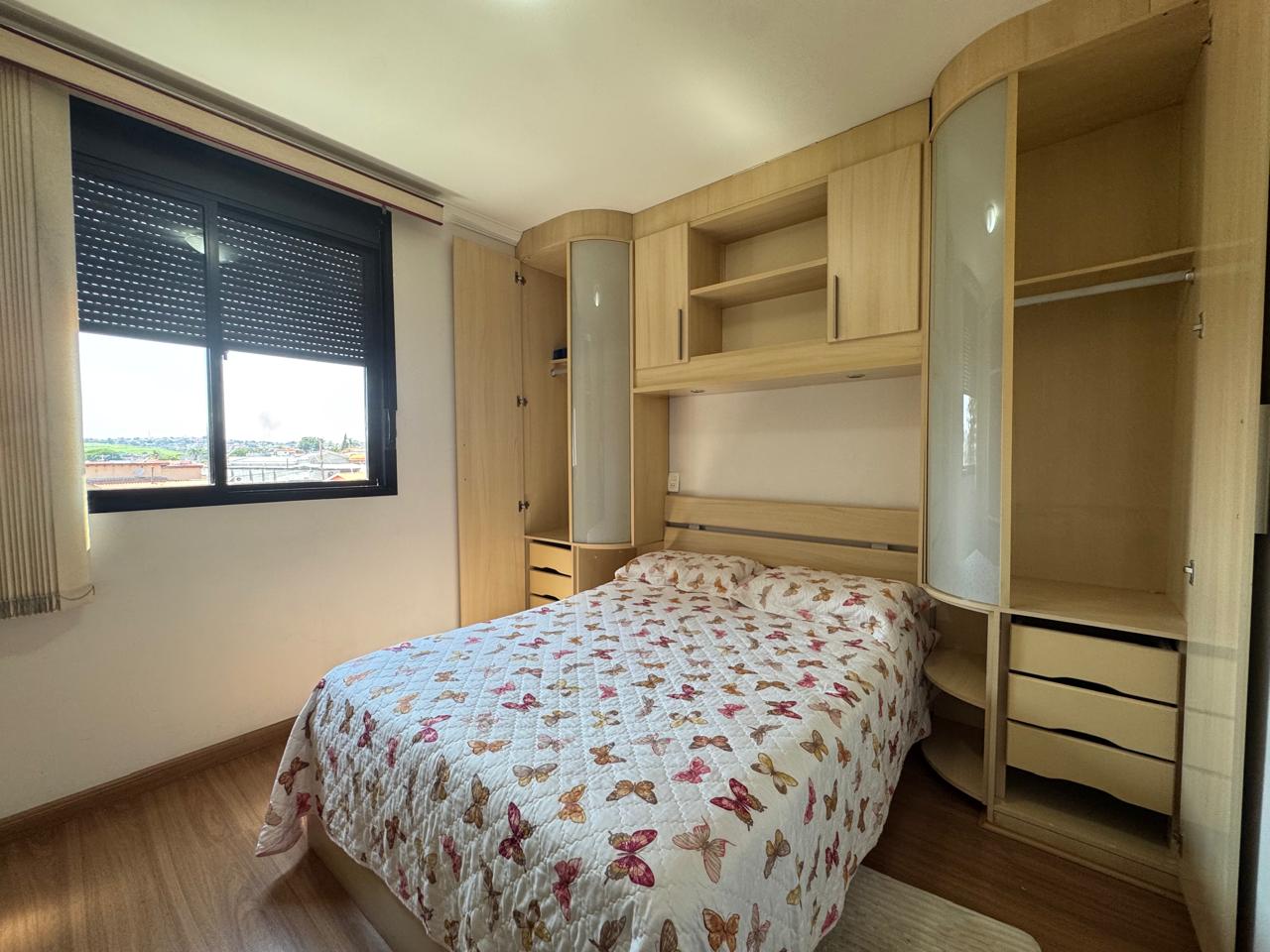 Vista frontal do quarto com móveis planejados em madeira ao redor da cama, piso laminado e janela com persiana